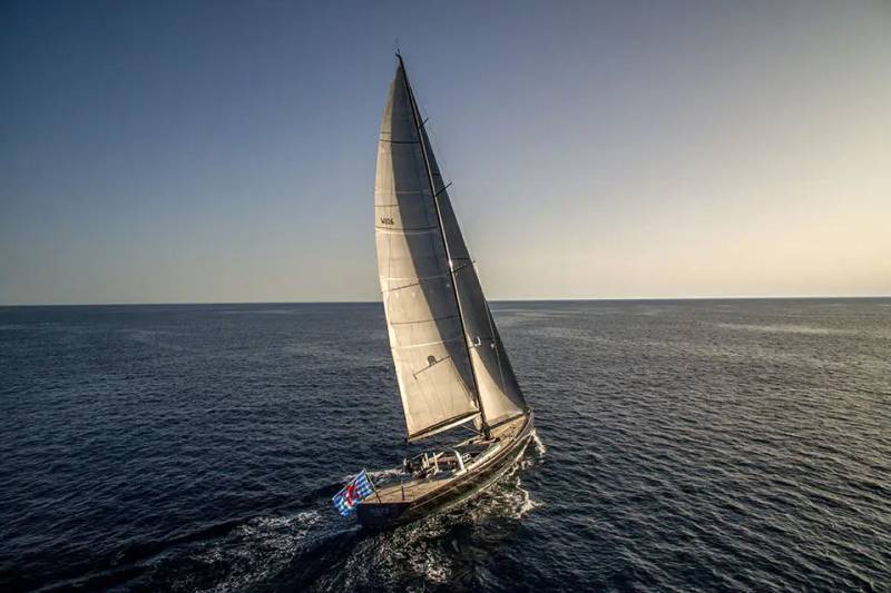 A sleek sailboat with full sails cuts through the deep blue ocean under a clear, bright sky.