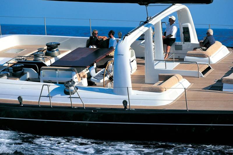 Four people relax on the deck of a large sailboat with the blue ocean stretching out behind them.