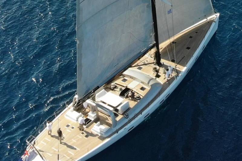 A sleek white sailboat with full sails glides across a deep blue ocean.
