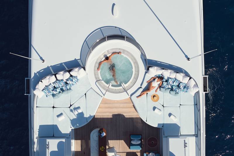 A couple relaxes in a jacuzzi on the deck of a yacht, with the deep blue ocean visible in the background.
