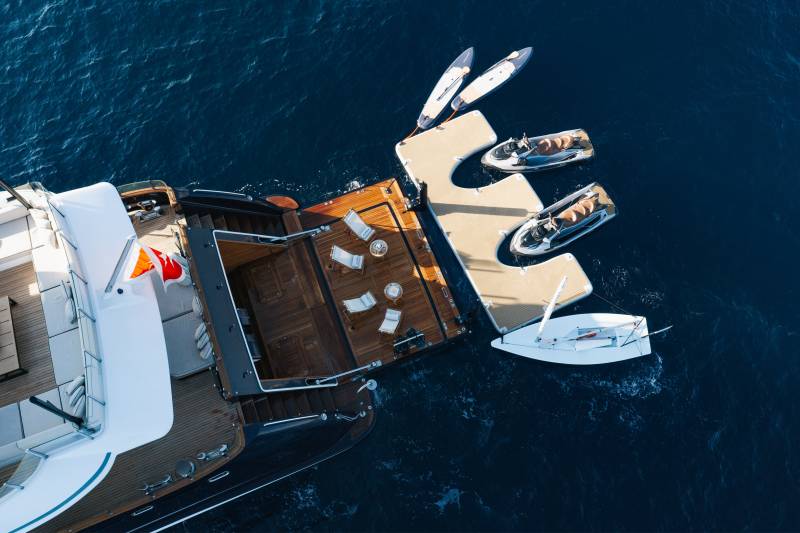 A luxury yacht with a wooden deck and lounge area sits in deep blue water, with a swim platform holding jet skis and paddleboards.