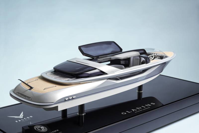 A sleek silver model yacht sits on a black display stand against a plain light blue background.