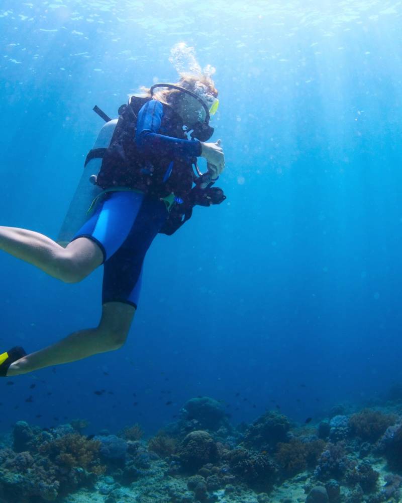 Scuba divers explore a vibrant coral reef bathed in the ethereal glow of sunlight filtering through the ocean's depths.