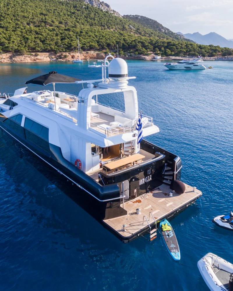 A luxurious yacht anchors in a serene bay, surrounded by lush green hills and sparkling blue waters.