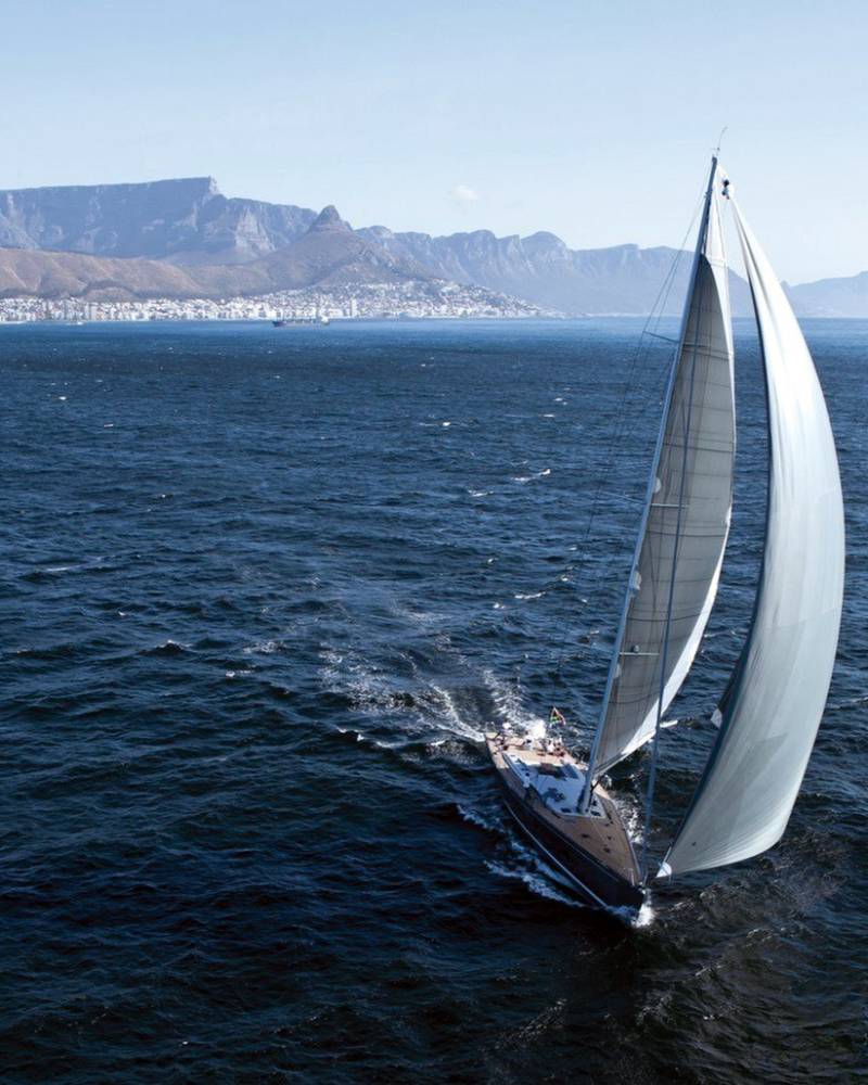 A majestic sailboat glides across the deep blue ocean with the iconic Table Mountain range in the distance.