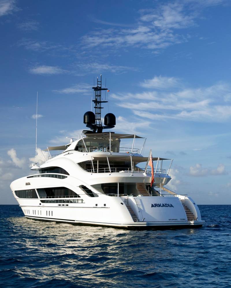 The luxurious superyacht Arkadia cruises serenely on the deep blue ocean under a vast sky dotted with clouds.