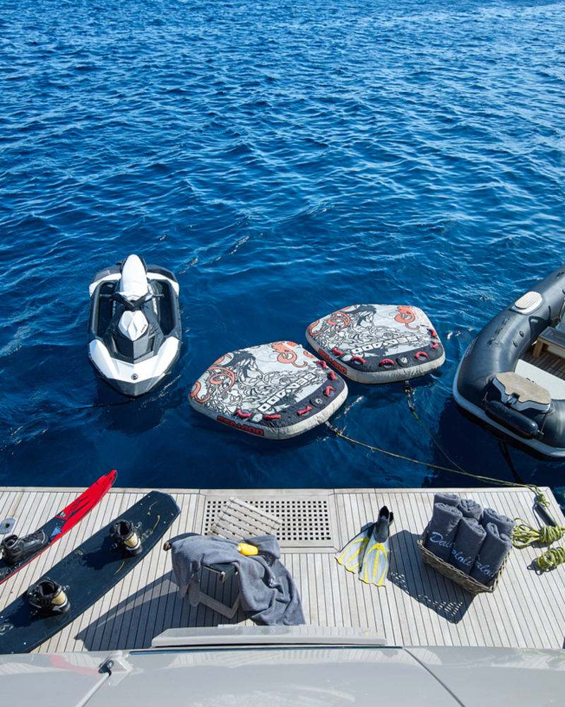A variety of water sports equipment, including a jet ski, inflatable tubes, and skis, are ready for adventure on the clear blue sea.