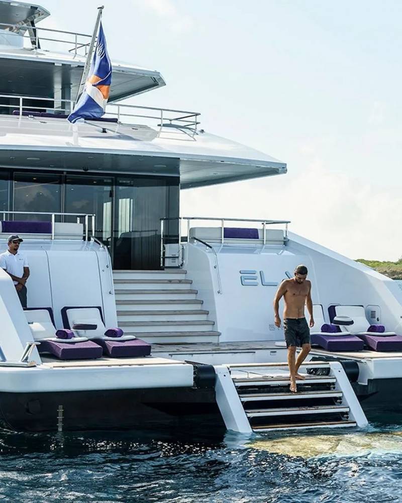 A man descends the steps of a luxurious yacht into the clear blue ocean waters.