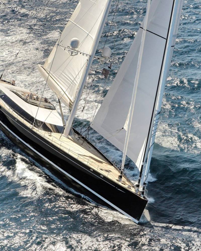 A sleek black yacht cuts through the sparkling blue ocean, its white sails billowing in the wind.