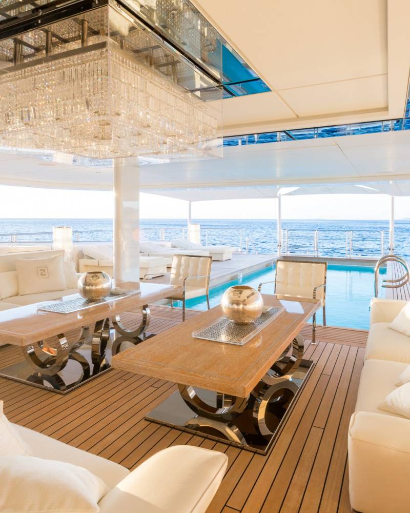 Luxurious white sofas and a crystal chandelier adorn this yacht's deck overlooking the tranquil blue ocean.