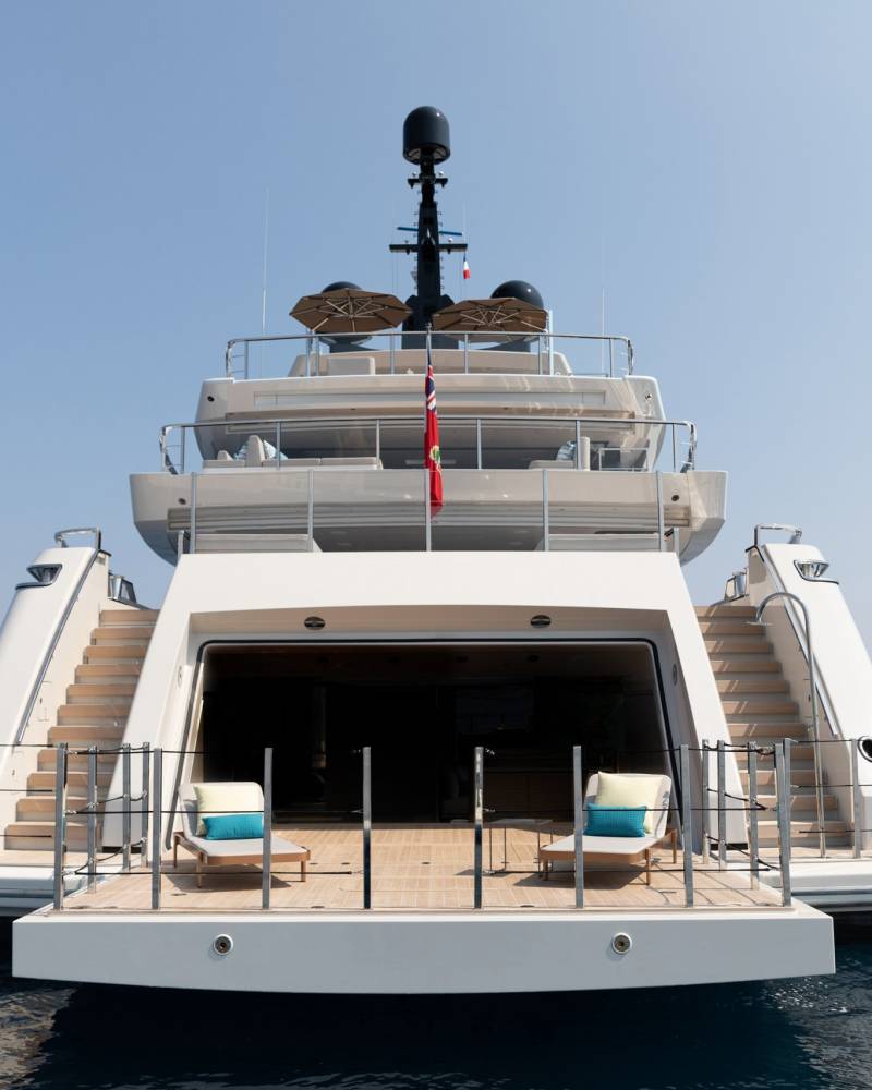 A luxurious yacht with open doors and lounge chairs awaits guests on a calm, blue sea.