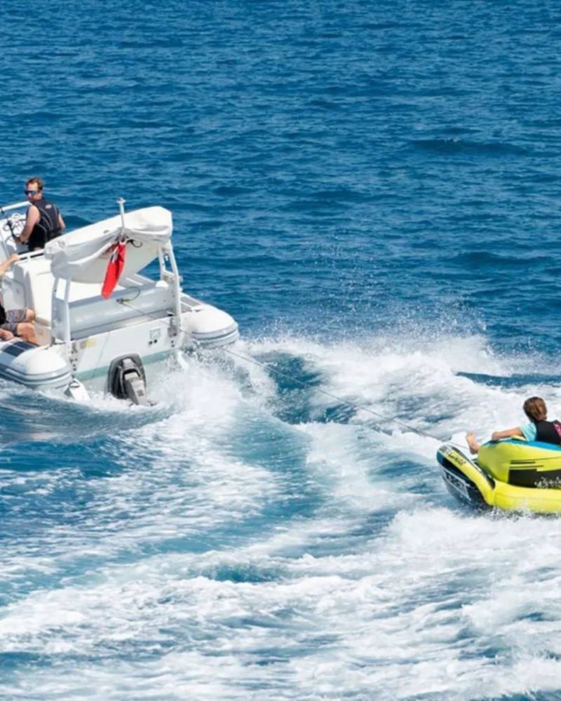 A speedboat tows a yellow inflatable tube with three people enjoying a sunny day on the ocean.