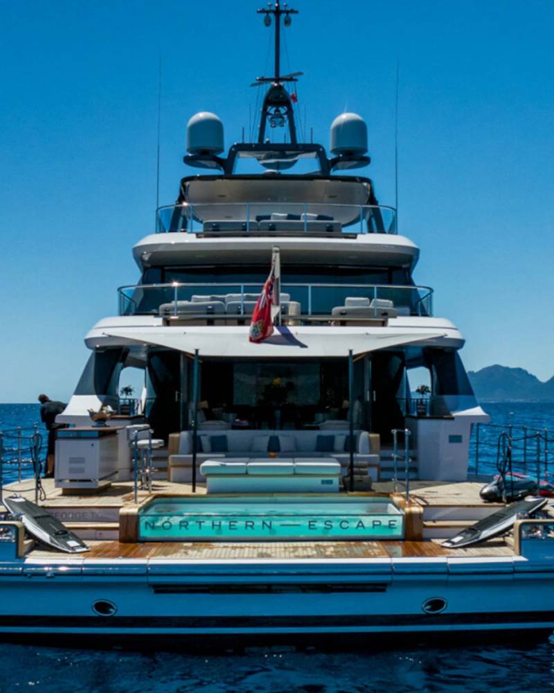 A luxurious yacht named "Northern Escape" cruises on a clear blue sea under a bright sunny sky.