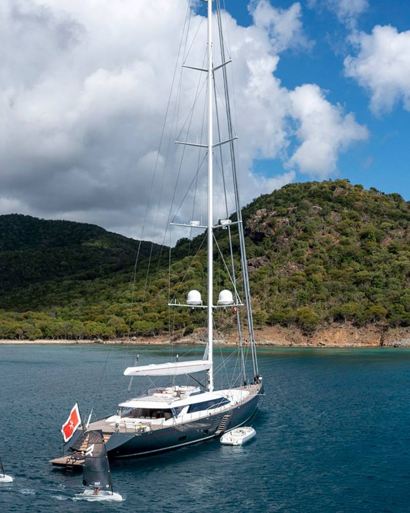 A majestic yacht sails serenely in clear blue waters near a lush, green island.