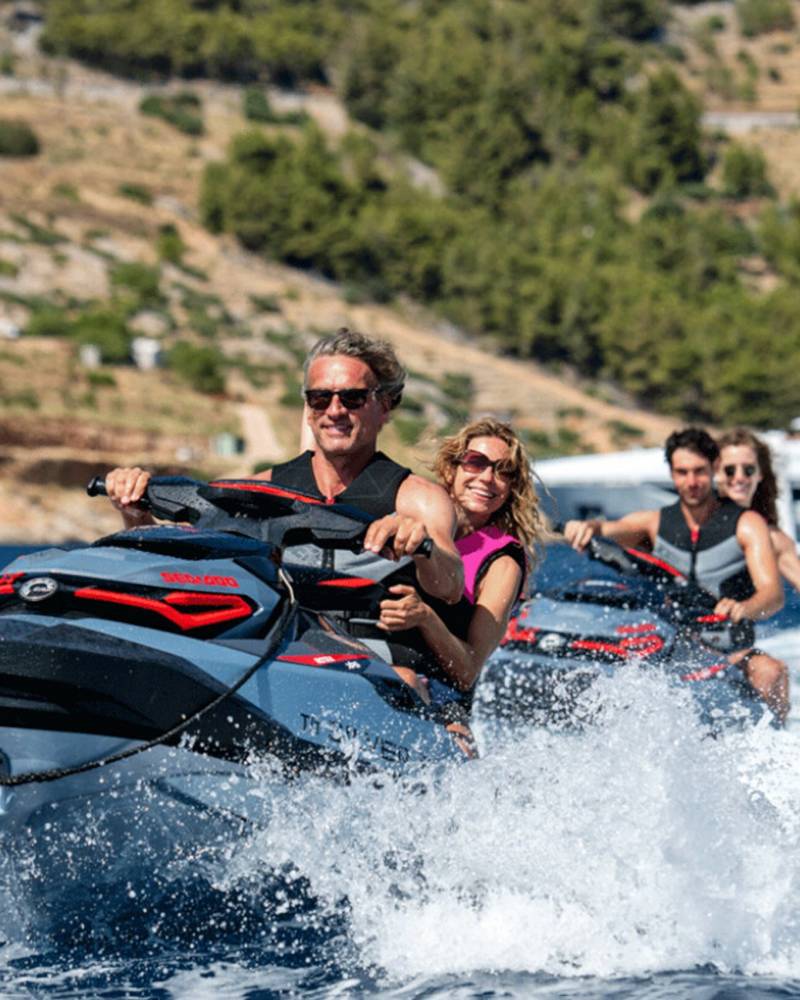 A group of friends enjoys a thrilling ride on jet skis in the clear blue waters with a luxury yacht in the background.