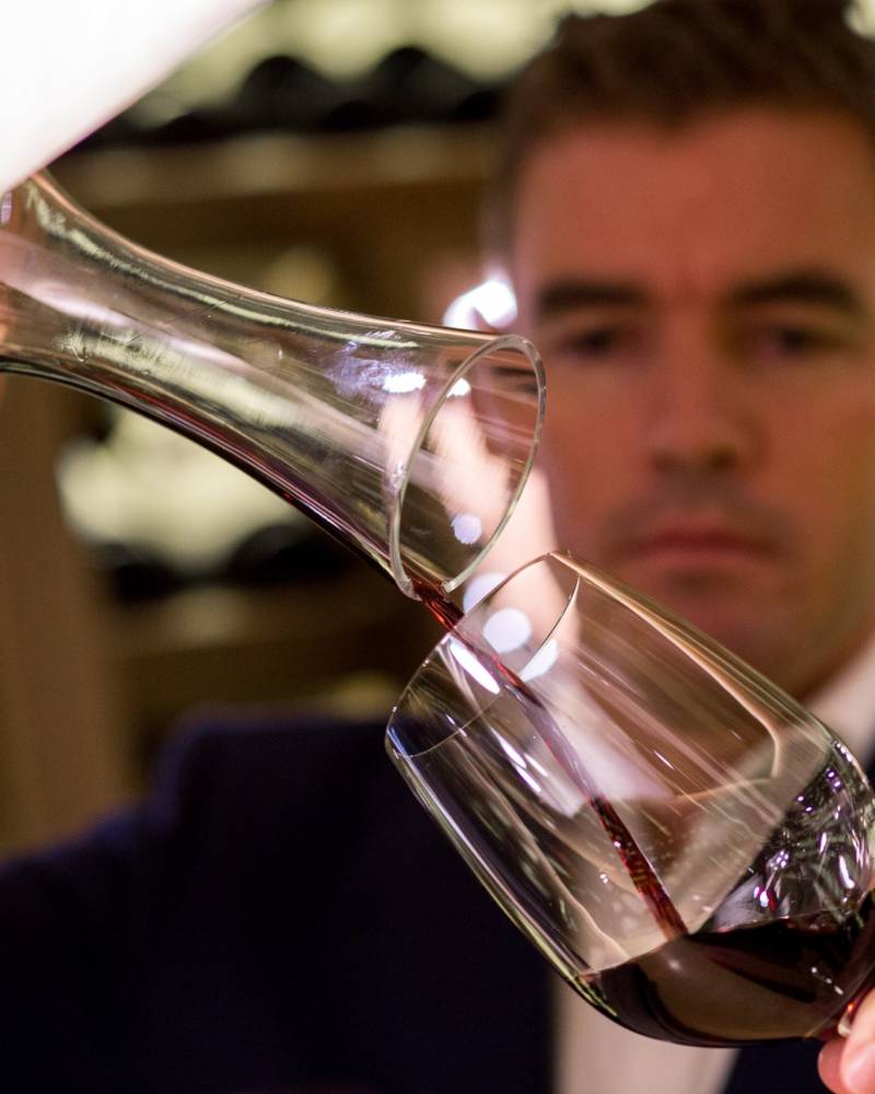 A sommelier carefully decants a rich red wine into a crystal glass in a dimly lit cellar.