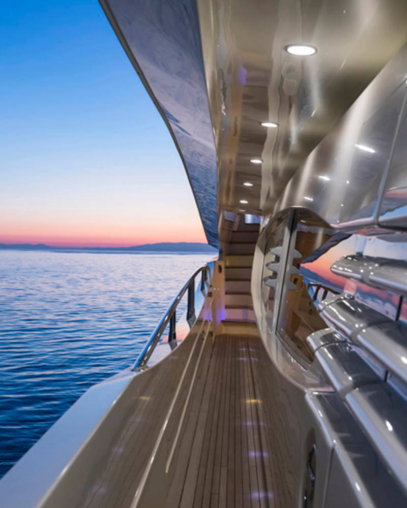 A luxury yacht's deck overlooking a serene ocean at sunset, with the horizon visible in the distance.