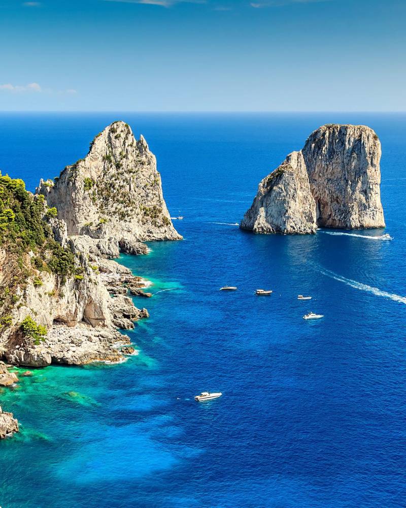 Boats dot the azure waters surrounding the dramatic cliffs and iconic sea stacks of Capri.