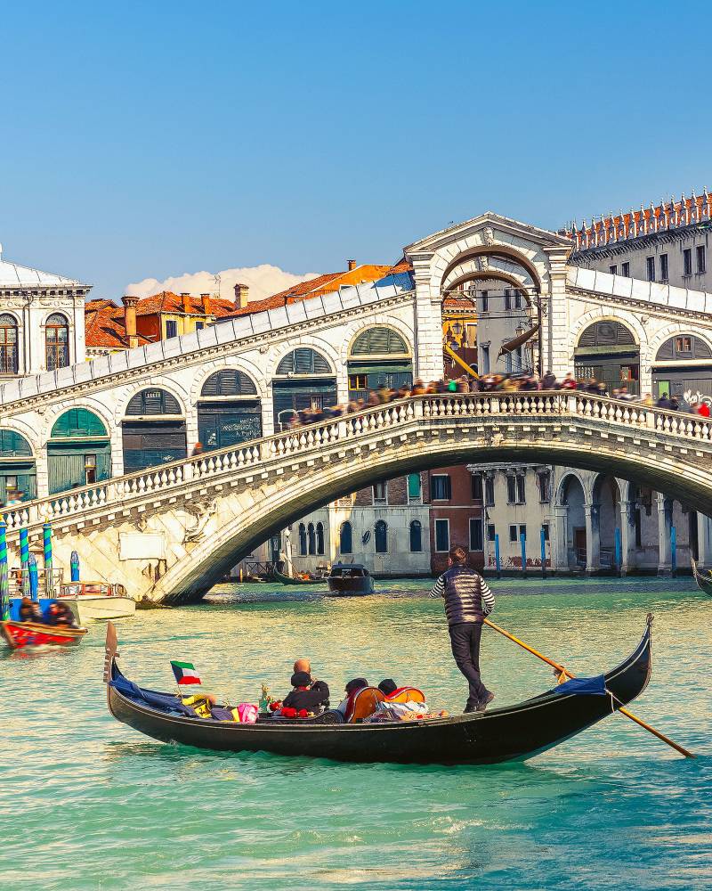 A gondola glides through the turquoise waters of Venice under the iconic Rialto Bridge.