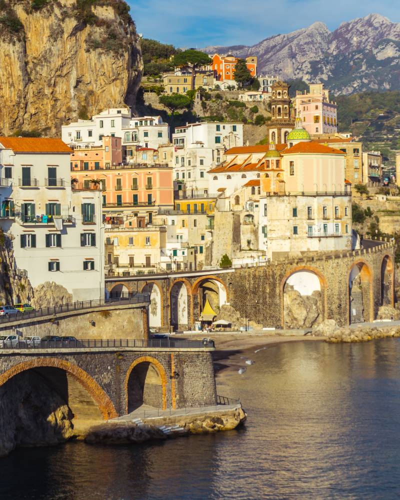 Colorful buildings cascade down a cliffside to a charming coastal town with ancient arched bridges.