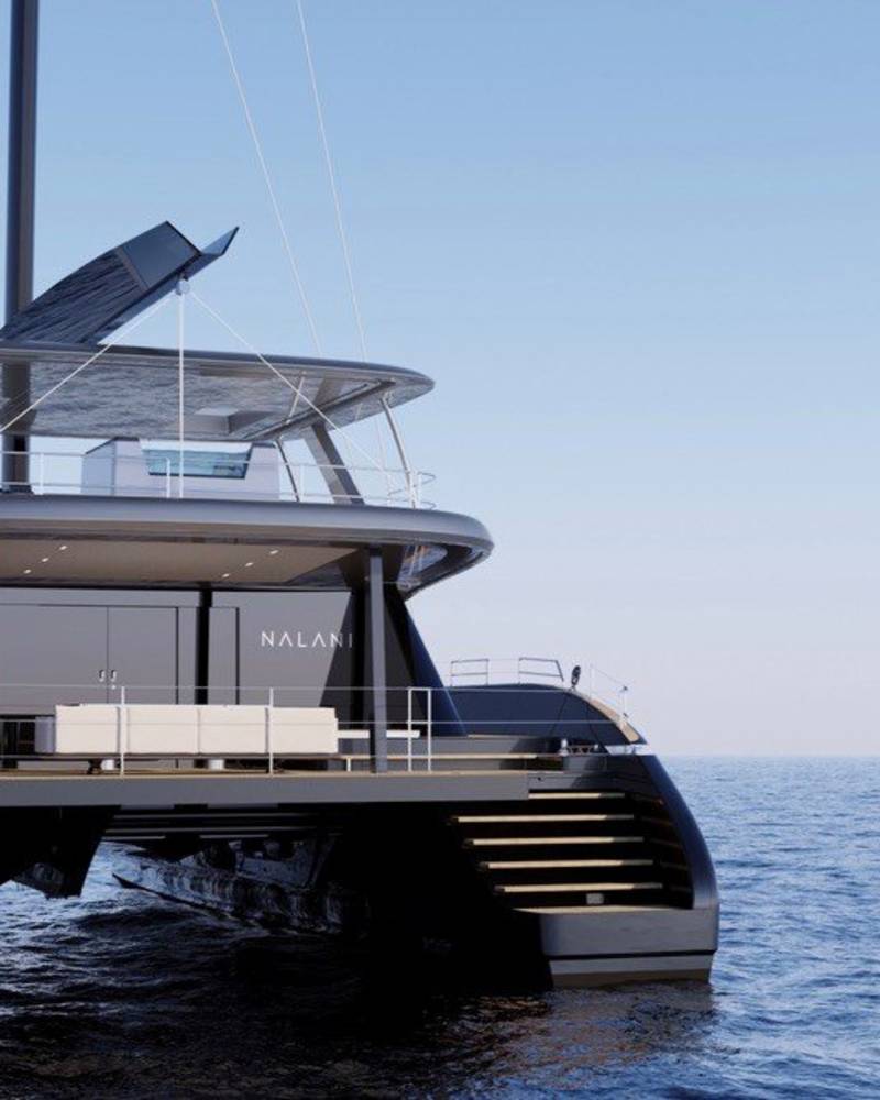 A sleek, modern catamaran yacht named Nalani glides across the calm, blue ocean under a clear sky.