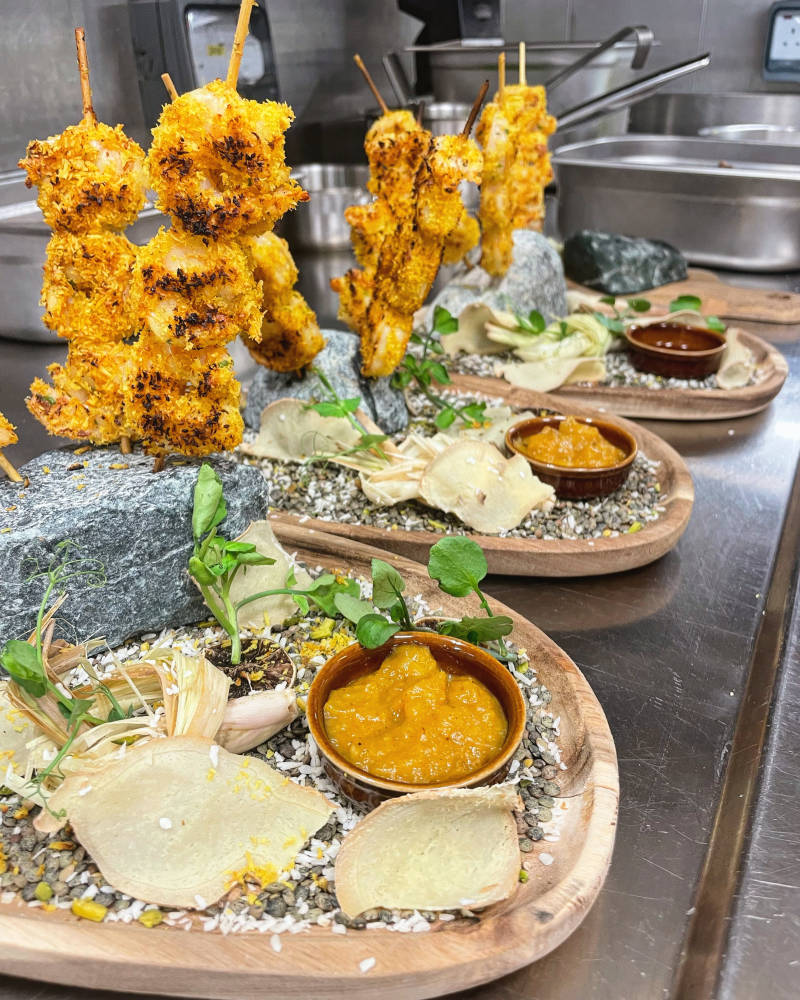 Crispy coconut-crusted shrimp skewers are artfully presented with vibrant dipping sauces and delicate garnishes on rustic wooden platters.
