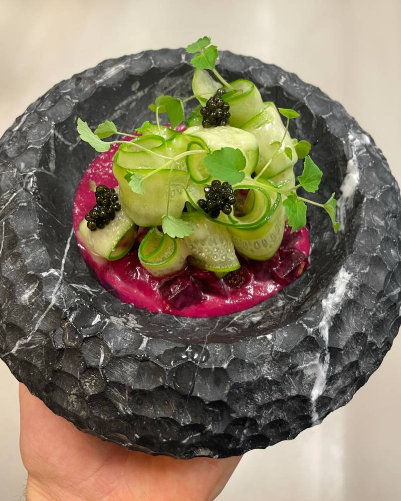 A delicate arrangement of cucumber rolls and caviar rests in a textured stone bowl, garnished with fresh microgreens.
