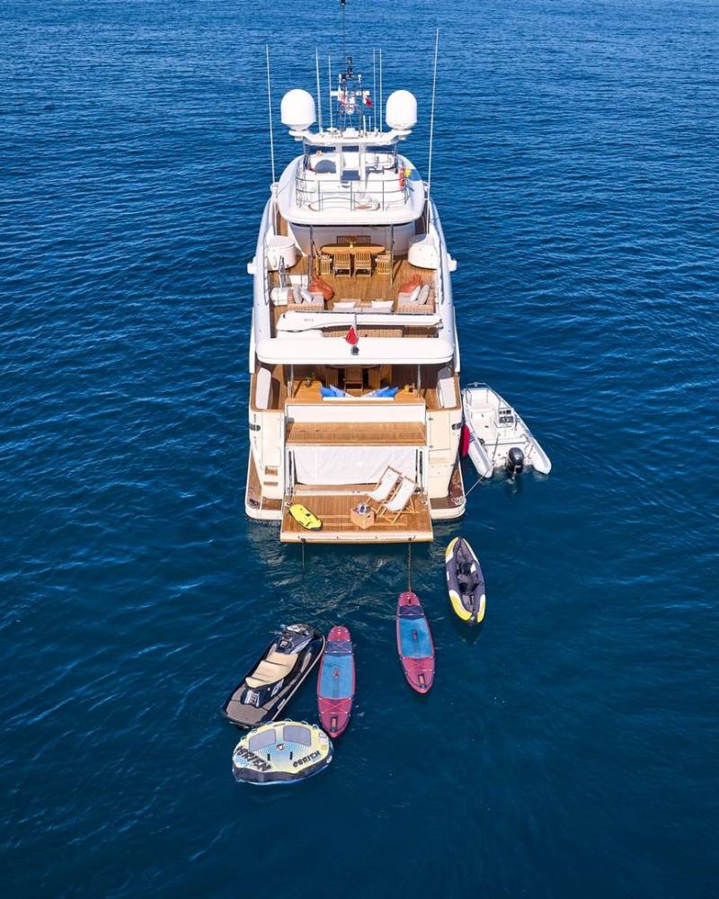 A luxurious yacht anchors in the deep blue sea, surrounded by inflatable toys and a tender.