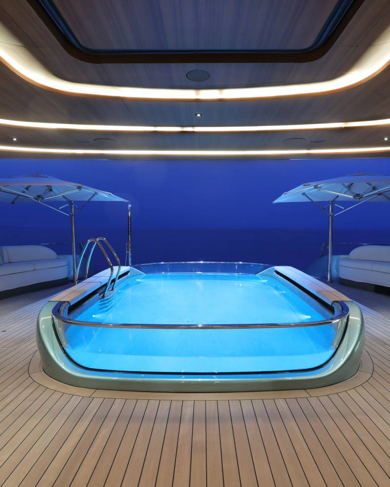 Luxurious yacht deck features a stunning illuminated pool overlooking the tranquil ocean at dusk.
