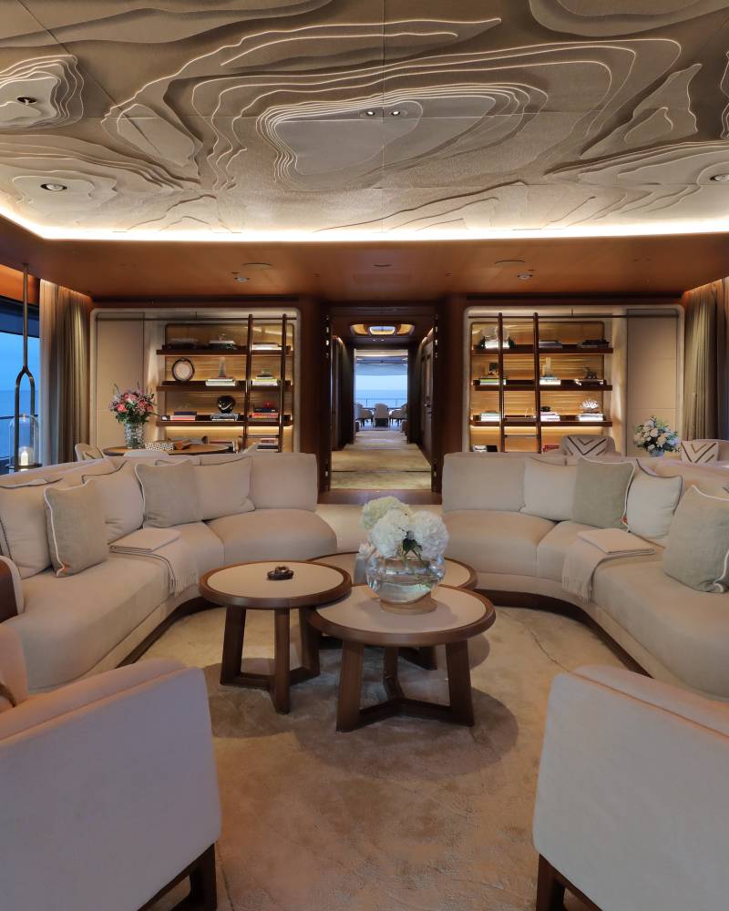 Luxurious yacht interior features a curved sectional sofa and a uniquely textured ceiling overlooking the serene ocean.