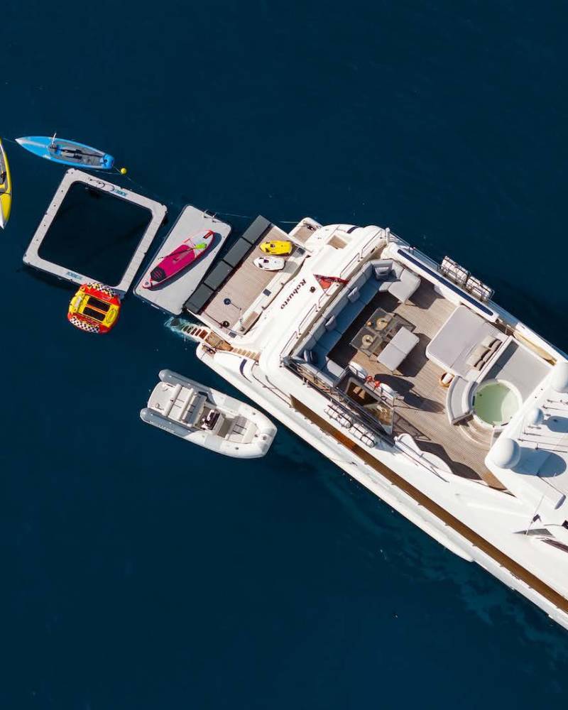 A luxurious yacht is anchored in deep blue waters, surrounded by various watercraft and a floating platform.