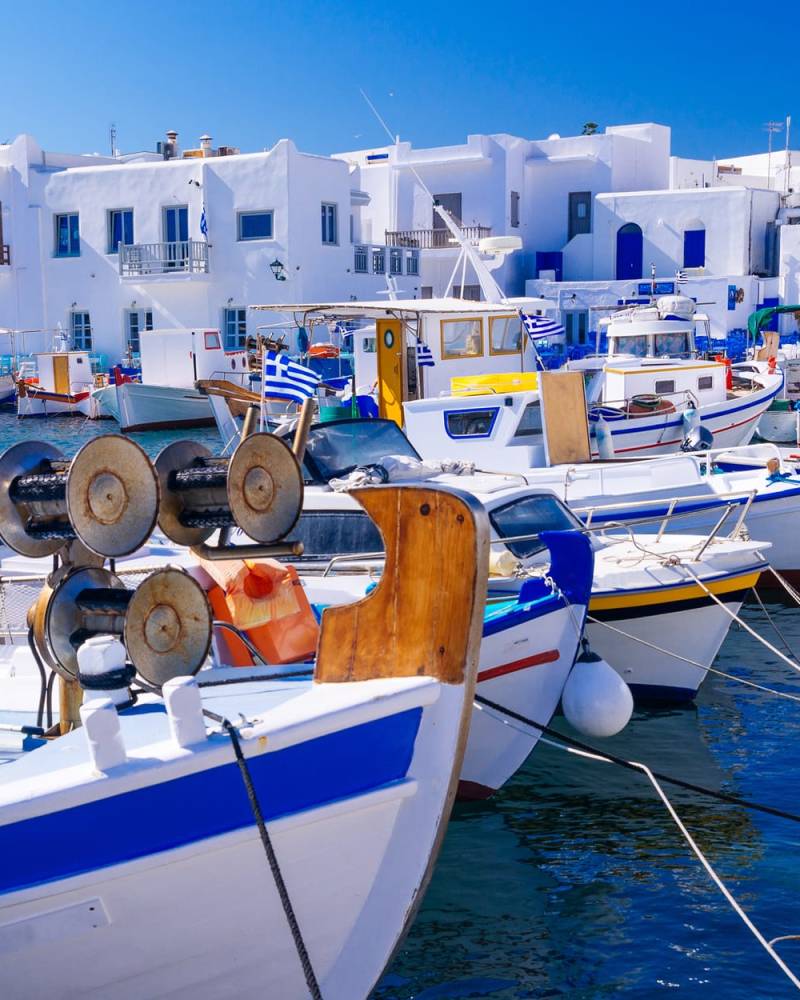 Fishing boats are moored along the waterfront in a picturesque Greek village under a clear blue sky.
