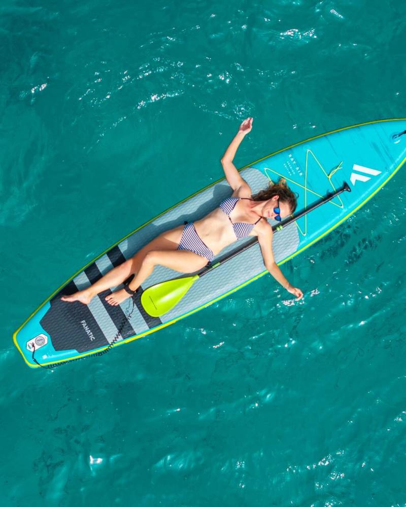 A woman in a striped bikini relaxes on a paddleboard in the crystal-clear turquoise waters of the ocean.