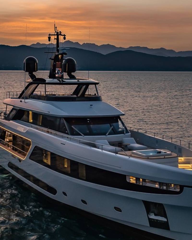 A luxurious yacht glides across calm waters at sunset, with silhouetted mountains in the distance.