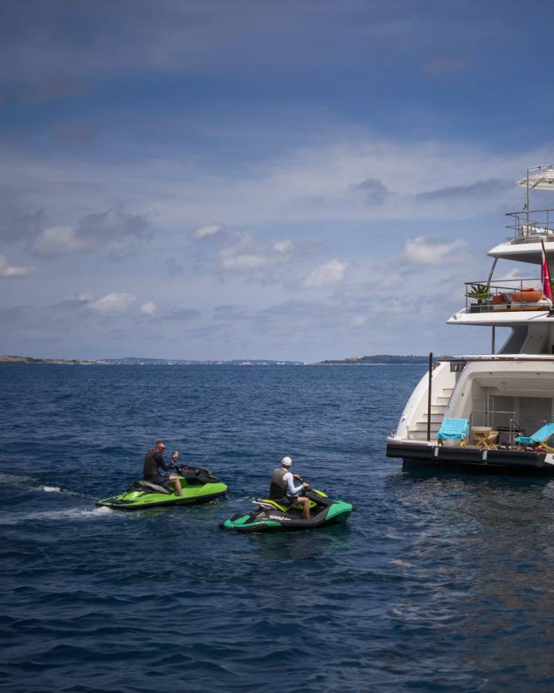 Two jet skiers enjoy a sunny day on the water near a luxurious yacht.