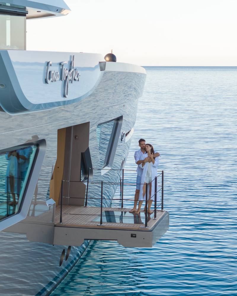 A couple embraces on the deck of a luxurious yacht as it glides across the calm, blue ocean.