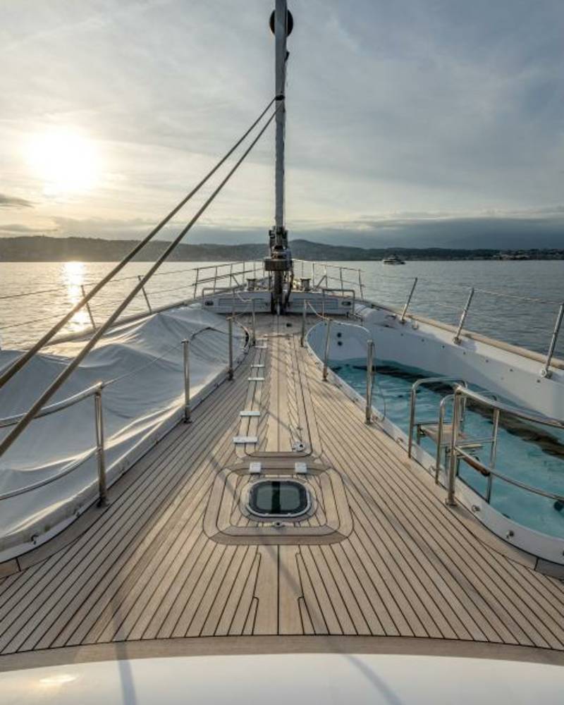 A luxurious yacht's deck offers a serene view of the sunset over the tranquil water with other vessels in the distance.