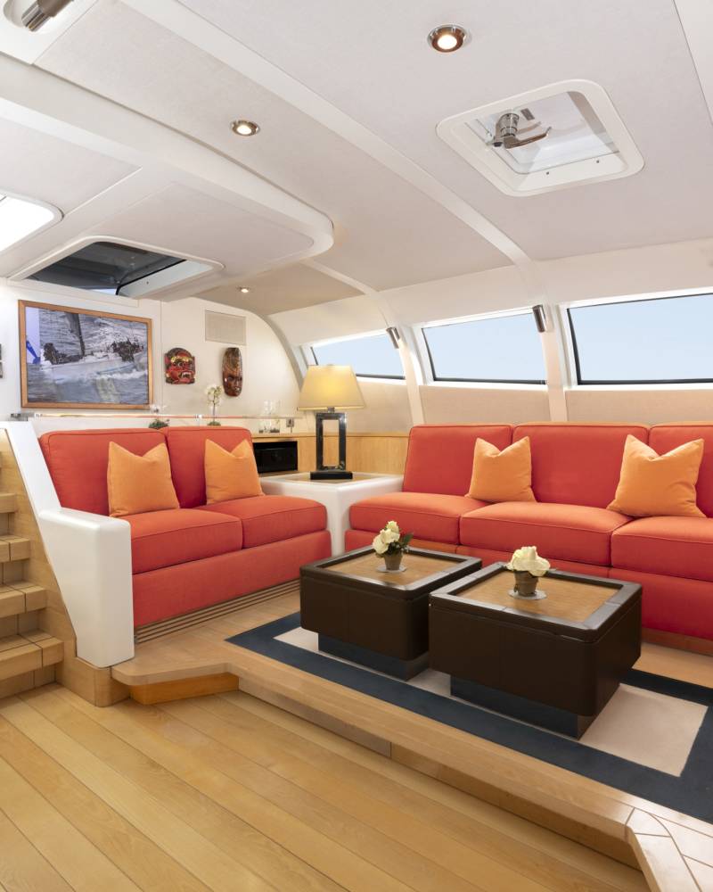 A spacious and modern living area with large, comfortable orange sofas, a wooden coffee table, and large windows providing natural light and a scenic view.