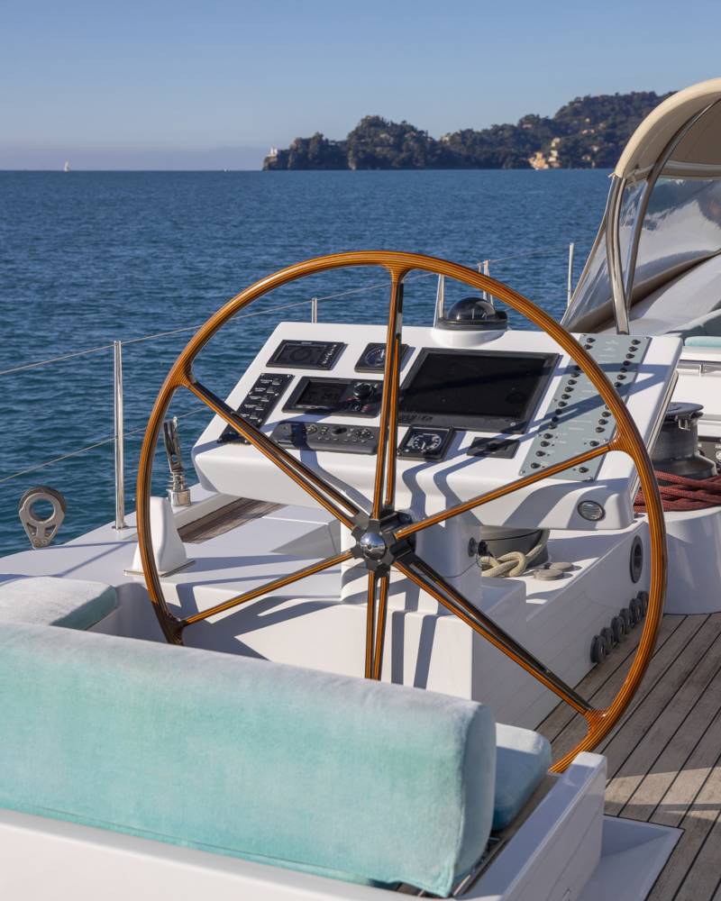 A luxurious yacht with a wooden steering wheel and a plush seating area overlooking a picturesque coastal town in the background.