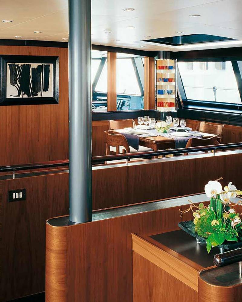 A luxurious yacht dining area features a polished wood interior, elegant table setting, and a striking modern artwork.