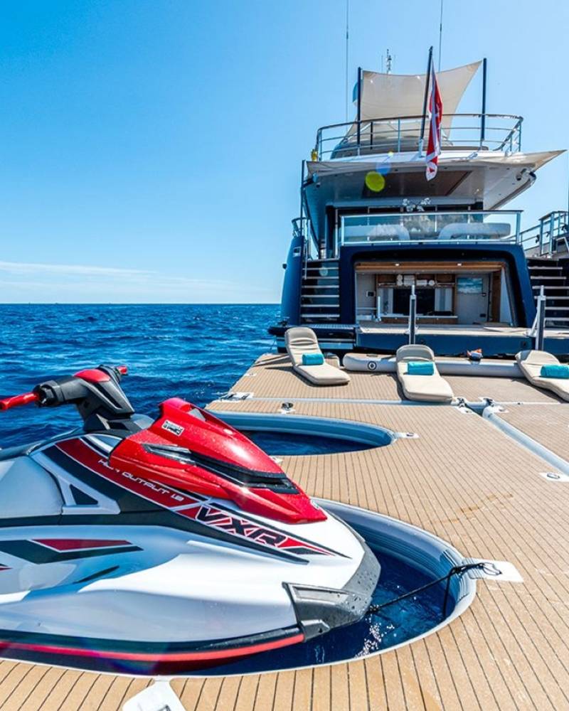 A sleek jet ski rests on a floating dock beside a luxurious yacht under a clear blue sky.
