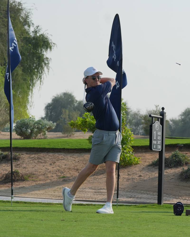 A golfer in mid-swing on a sunny day at a desert golf course.