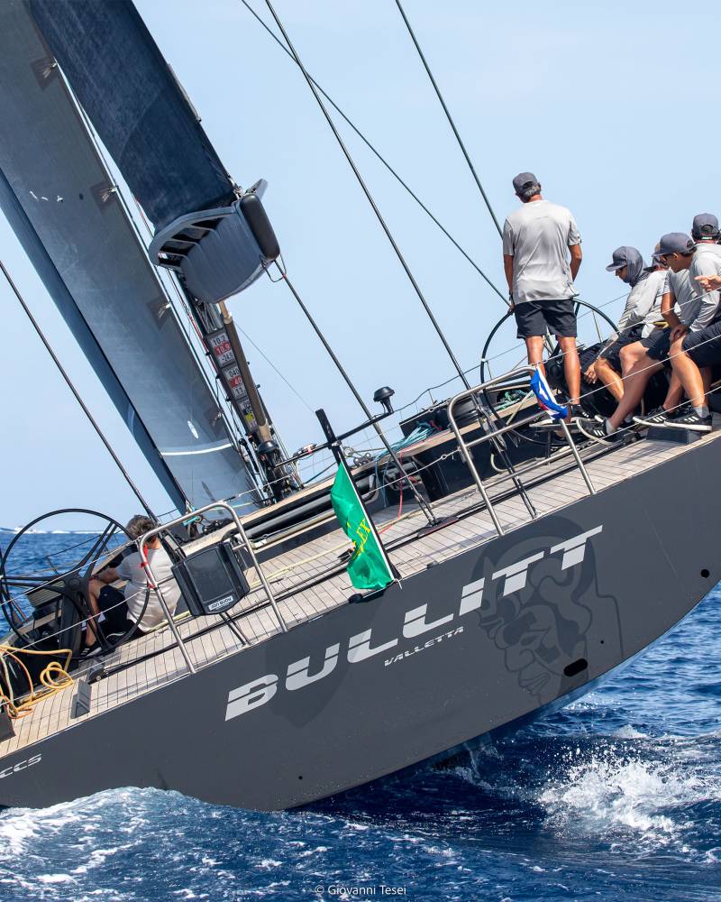 A sleek sailboat cuts through the deep blue ocean waves, its crew focused on the race ahead.