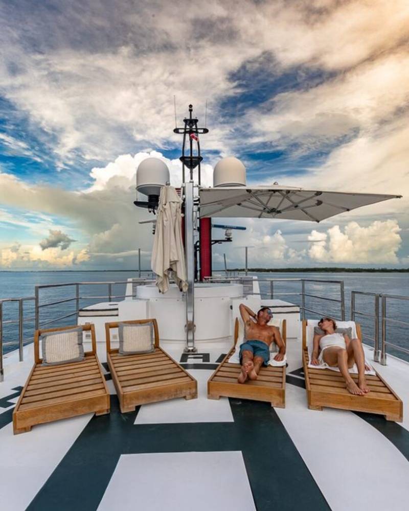 A couple relaxes on lounge chairs on the deck of a yacht, enjoying the expansive ocean and dramatic sky.