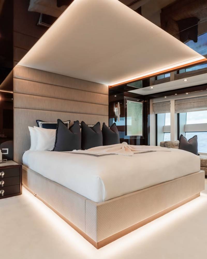 A spacious and modern bedroom with a large bed, minimalist furniture, and floor-to-ceiling windows offering a scenic view of the surrounding environment.