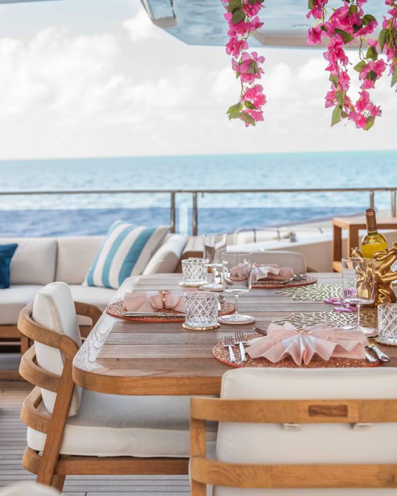 A beautifully decorated outdoor dining area overlooking a serene ocean view, with a wooden table set with elegant tableware and surrounded by comfortable seating.