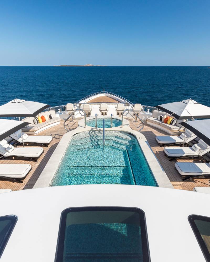 Luxurious loungers and a sparkling pool await on the deck of this magnificent yacht, set against a backdrop of the serene blue sea.