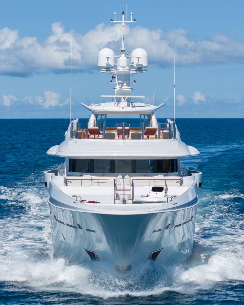 A sleek white yacht cuts through the deep blue ocean, leaving a foamy wake under a bright, cloudy sky.