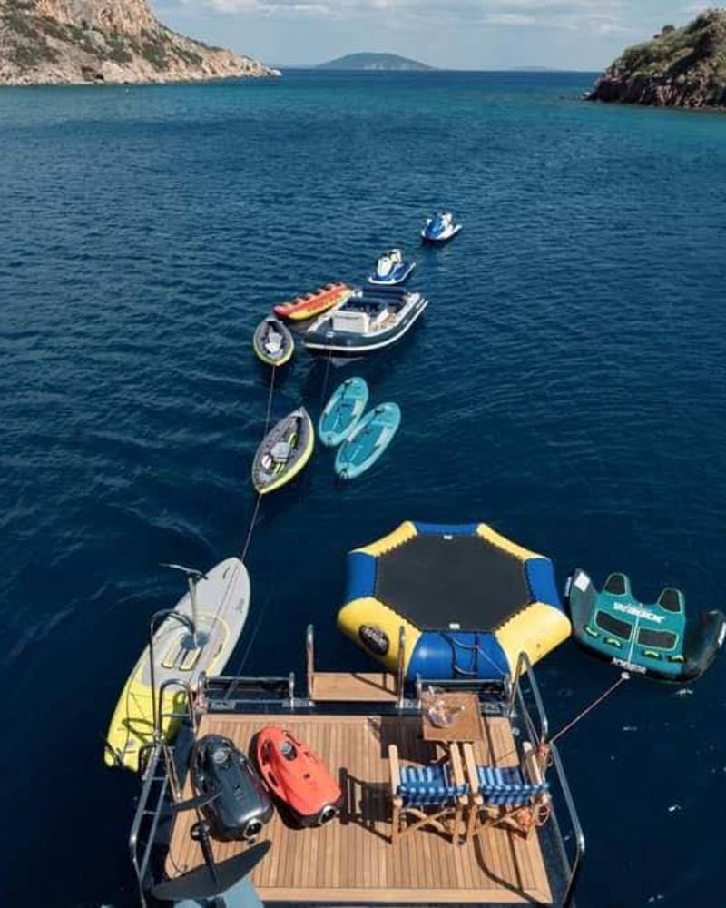 A luxury yacht anchors in a serene bay, surrounded by an array of water toys and inflatable fun.