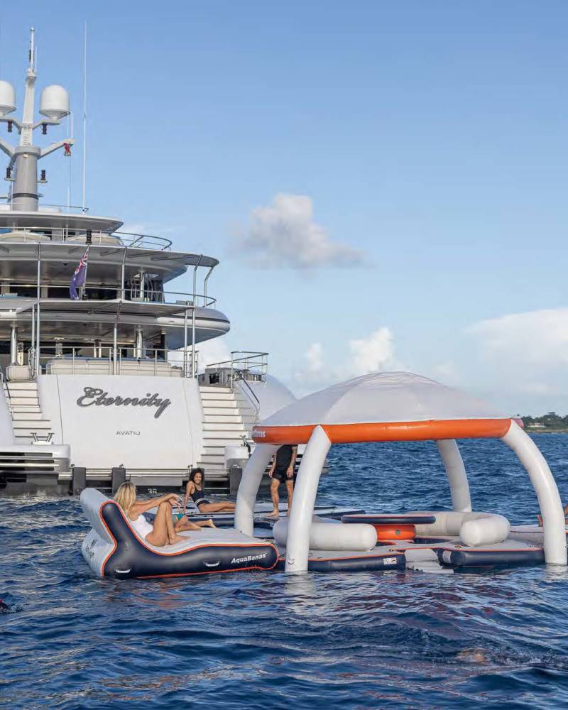 Luxury yacht "Eternity" anchors offshore, providing a stunning backdrop for a floating inflatable island lounge and water sports.